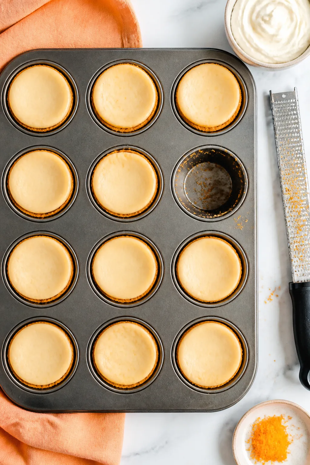 Overhead “tasty top view”: A muffin tin filled with 12 orange creamsicle mini cheesecakes right