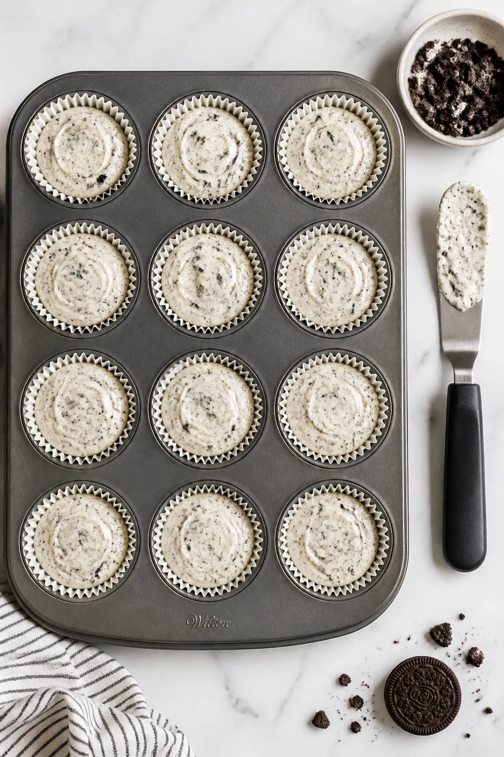 Overhead process shot of a 12-cup muffin tin lined with paper liners, each cup filled evenly with th