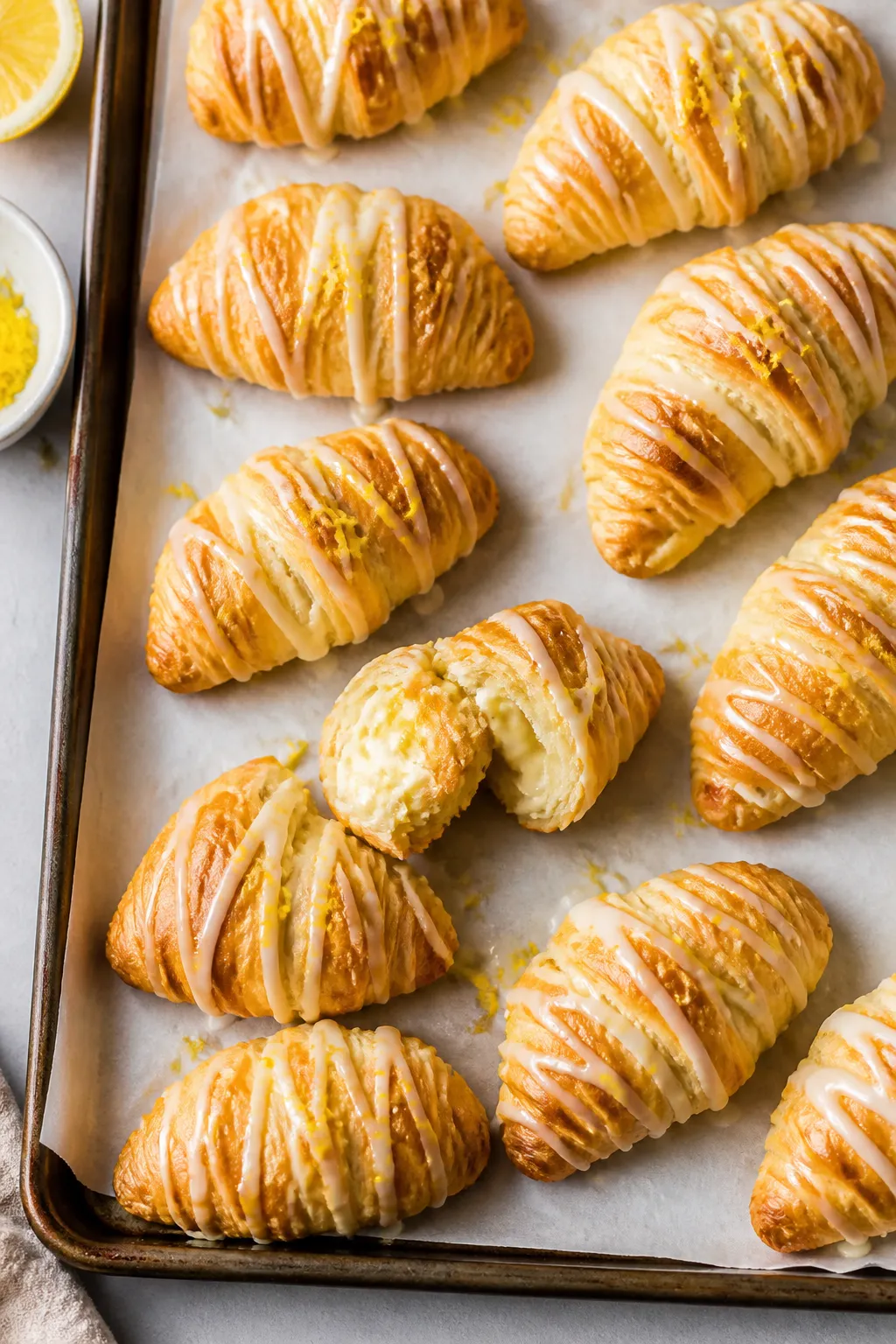 Overhead shot of freshly baked lemon cheesecake crescent rolls cooling on a parchment-lined baking s
