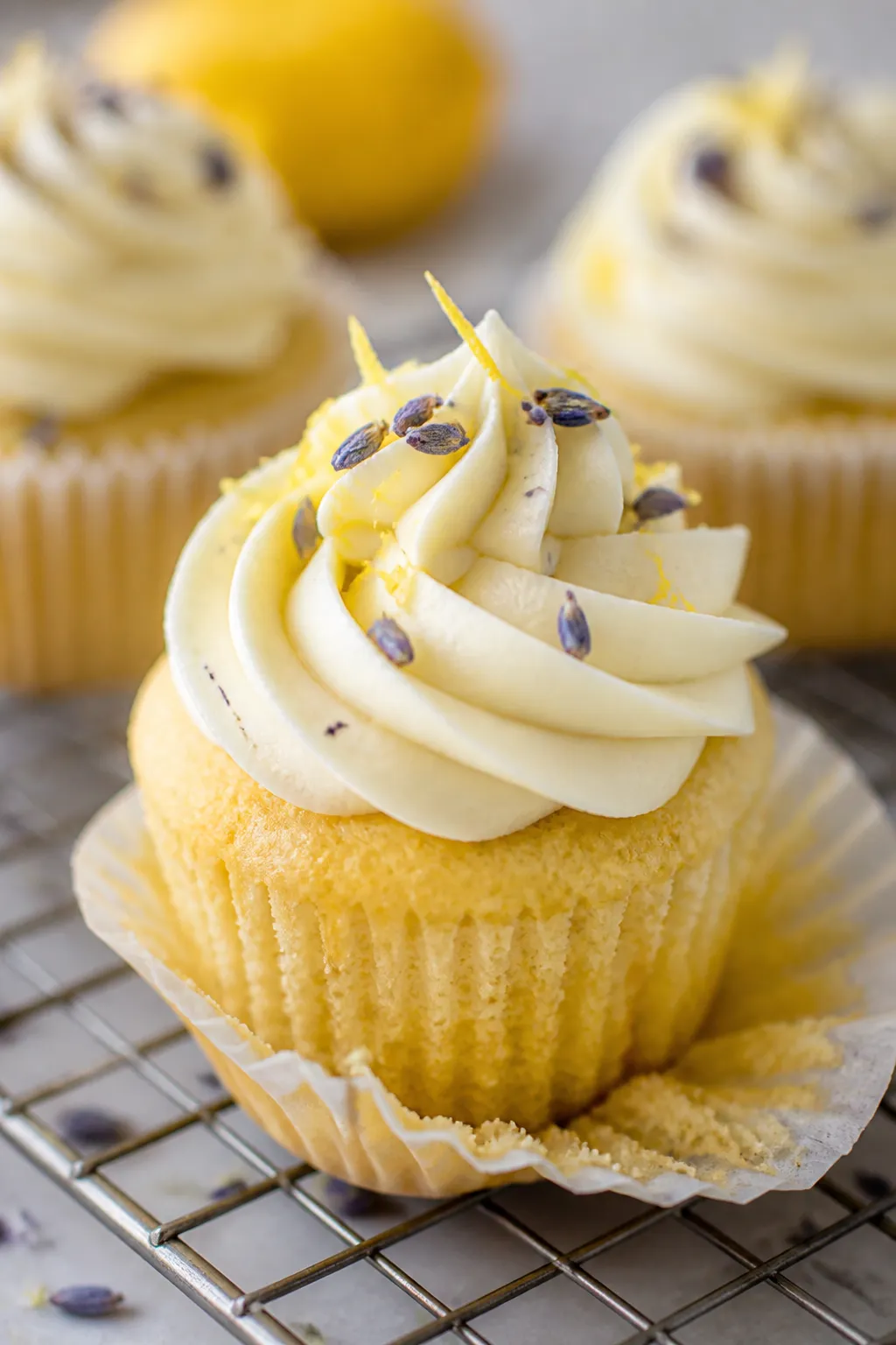 Close-up detail shot: A freshly frosted lemon lavender cupcake on a wire rack, silky lemon cream che