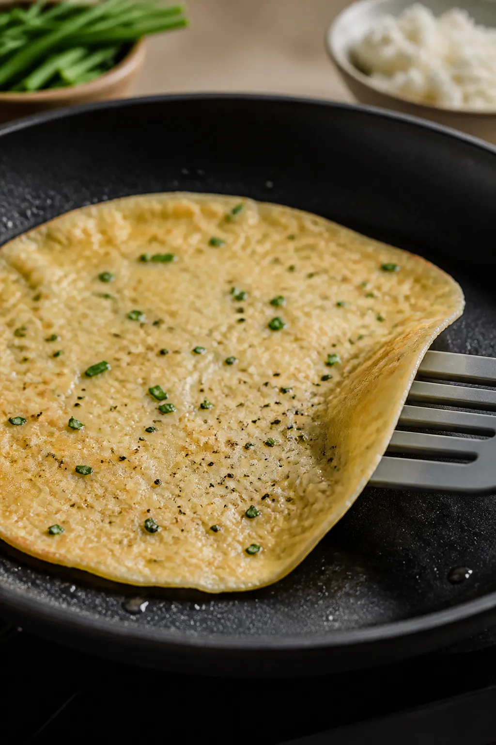 Cooking process close-up: A thin egg and cottage cheese flatbread cooking in a nonstick skillet over